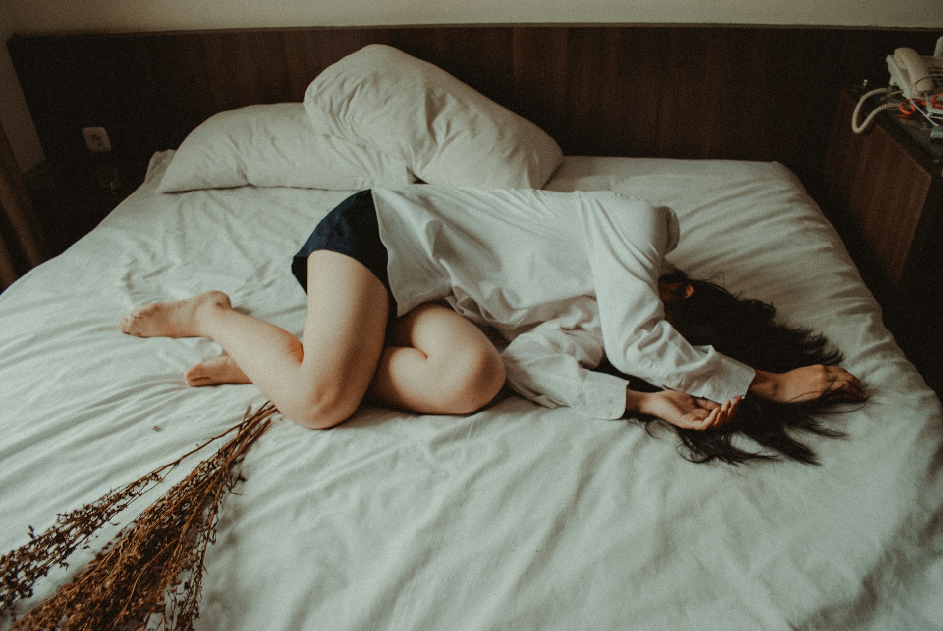 Personne allongée en boule sur un lit avec un rhume, portant une chemise et un short.