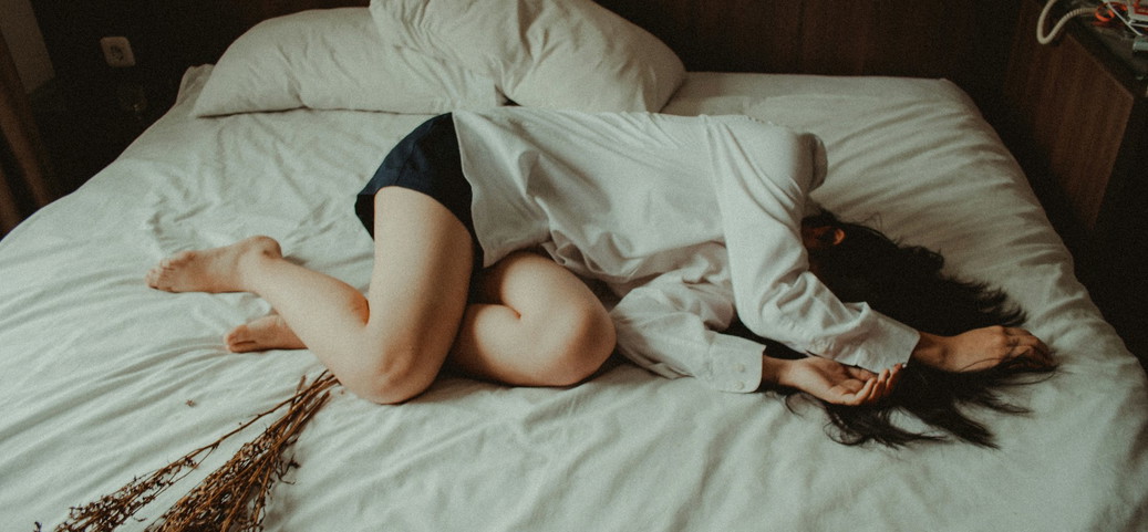Personne allongée en boule sur un lit avec un rhume, portant une chemise et un short.