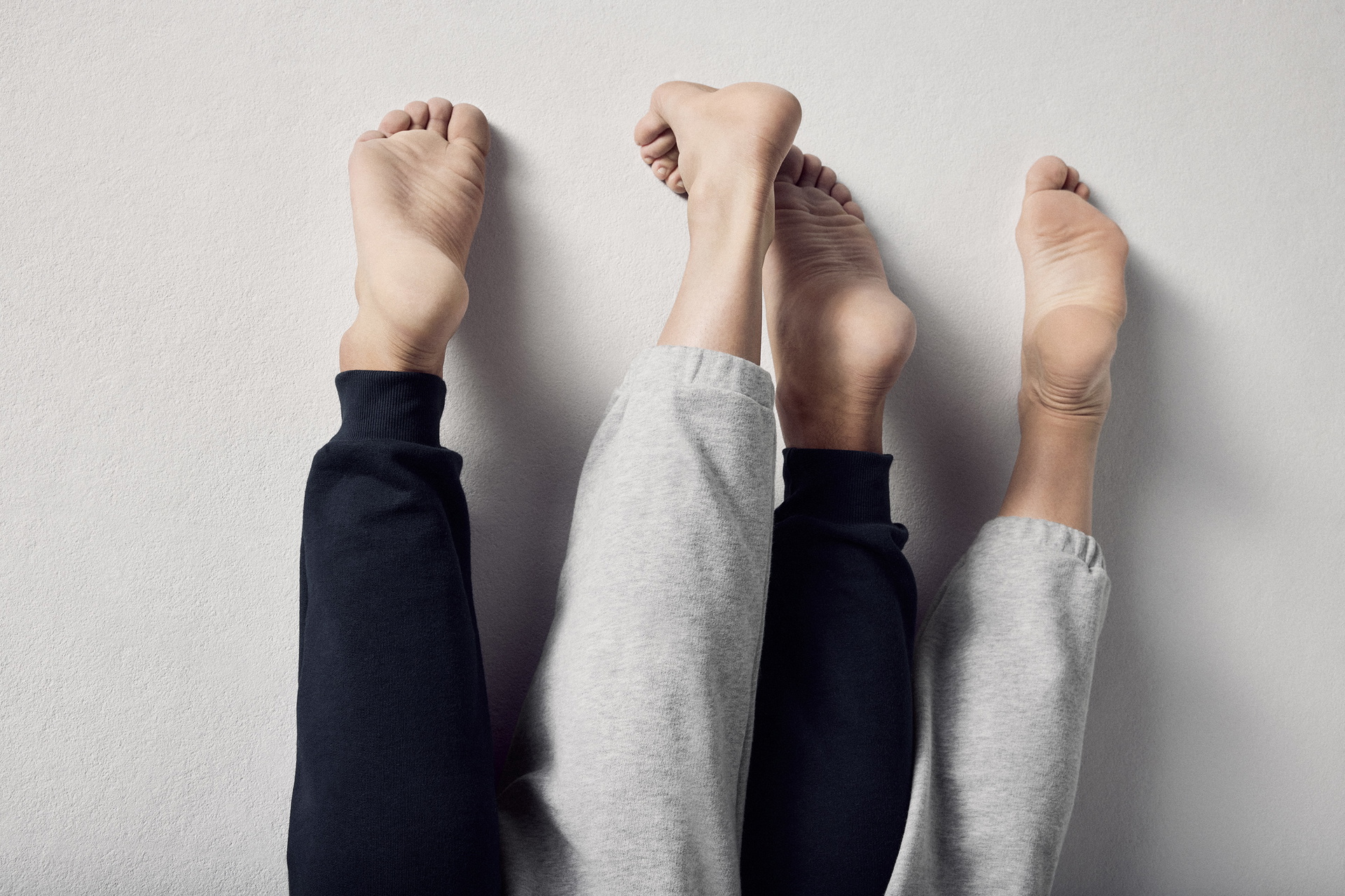 Deux paires de pieds nus en pantalon de jogging sont posées côte à côte sur une surface claire.