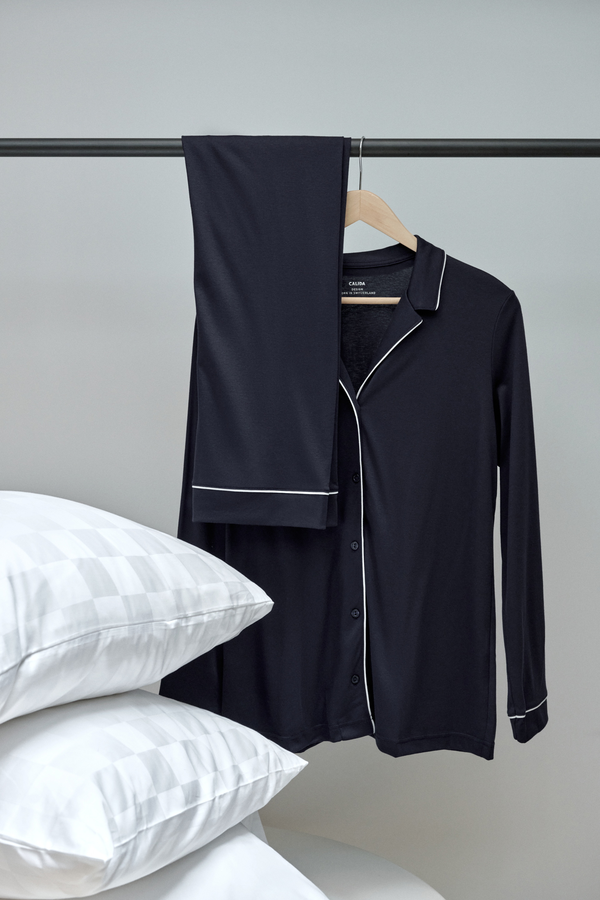 Pyjamas CALIDA bleu foncé avec boutons de la série Night Lovers, soigneusement exposés sur un cintre avec des oreillers