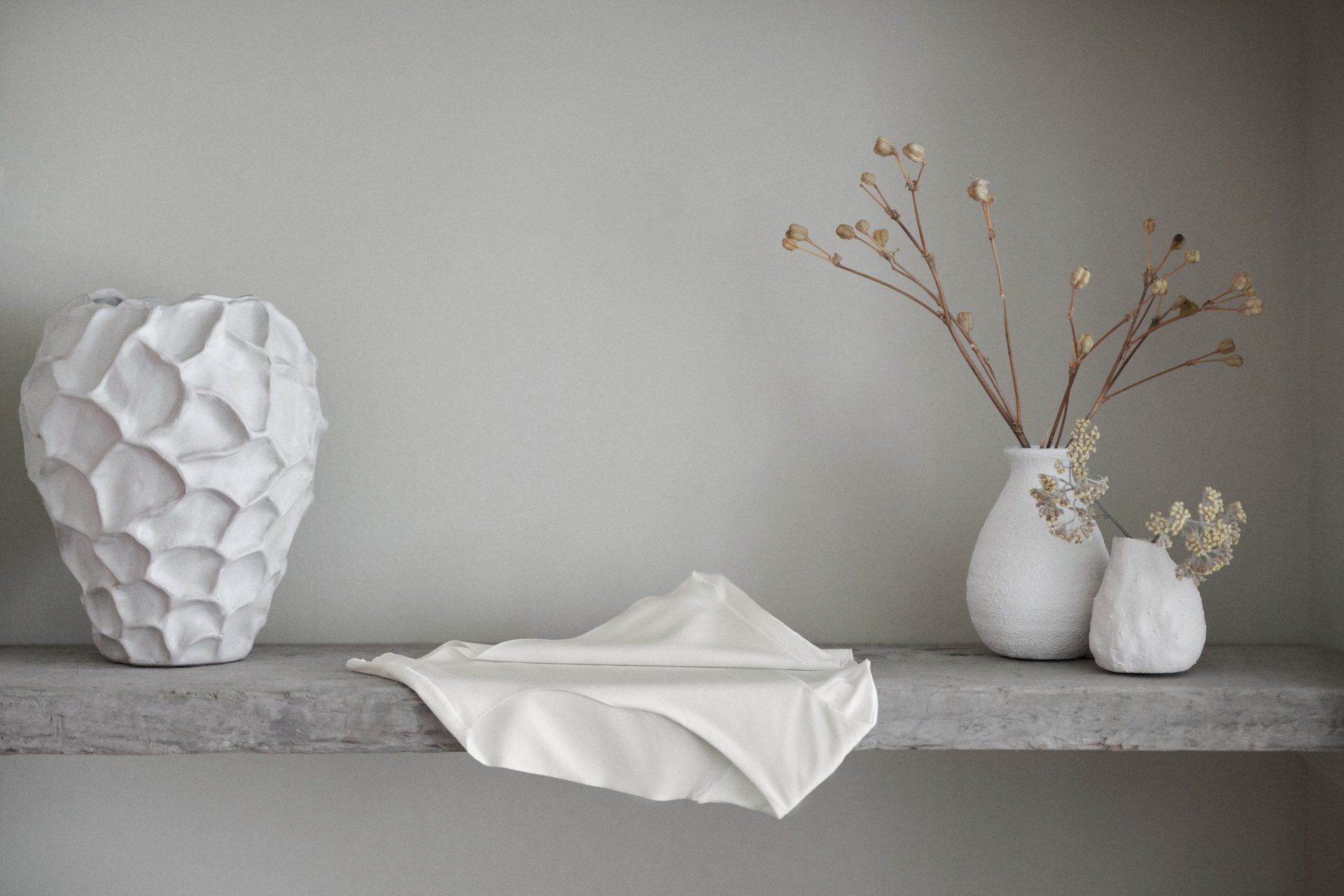 Minimalistische Deko‑Szene mit weissen Vasen und Stoff auf grauer Ablage; im Vordergrund liegt ein CALIDA Seamless‑Midi‑Slip aus der Serie Natural Skin
