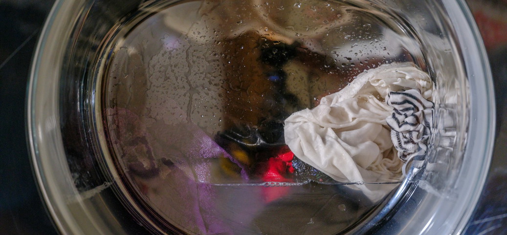 Close-up of a washing machine drum containing wet, white and coloured clothing. Drops of water are visible on the inside of the drum.