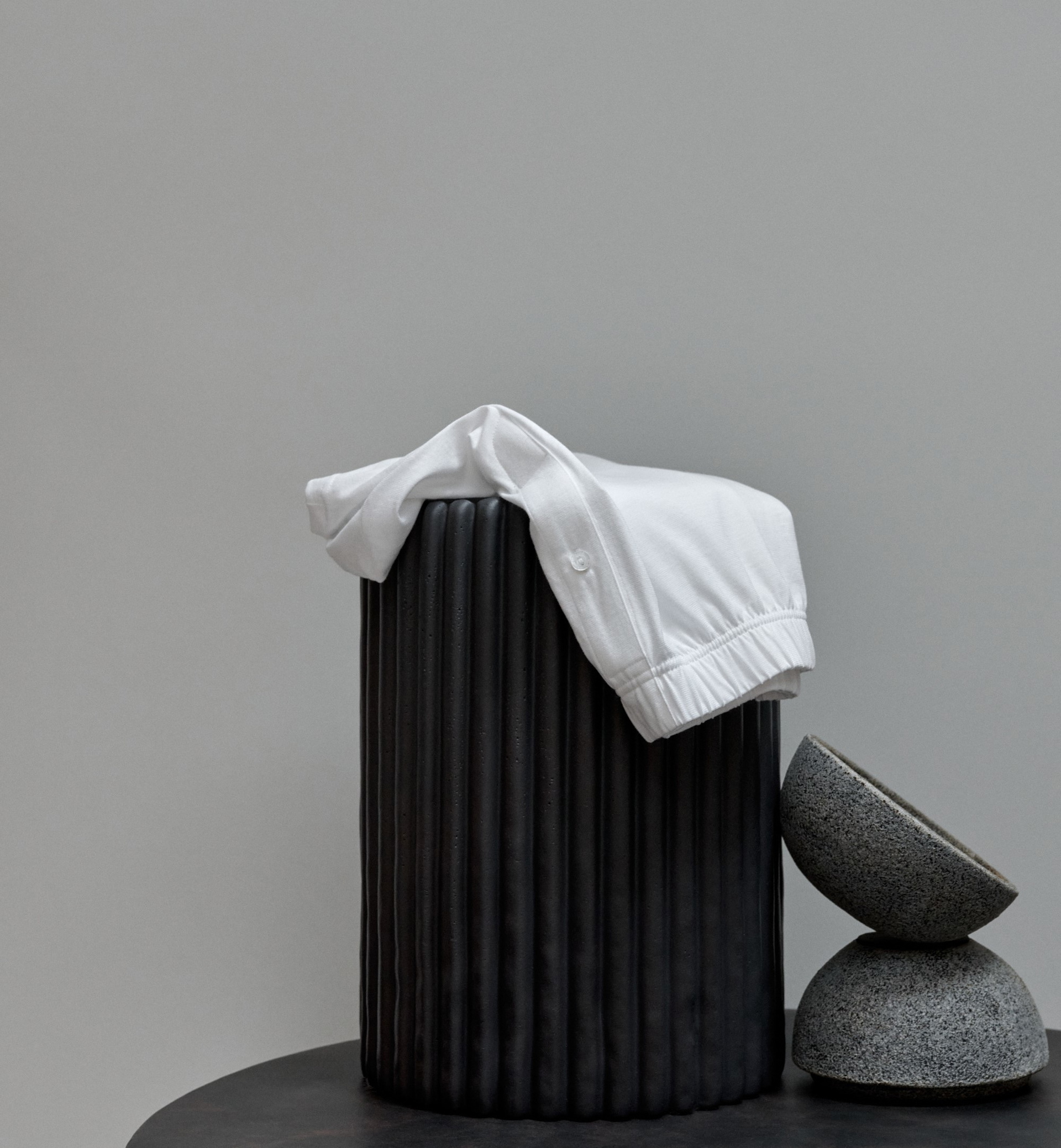 The picture shows a white item of clothing draped over a black, cylindrical object. Next to it are two grey, bowl-shaped objects stacked on top of each other.