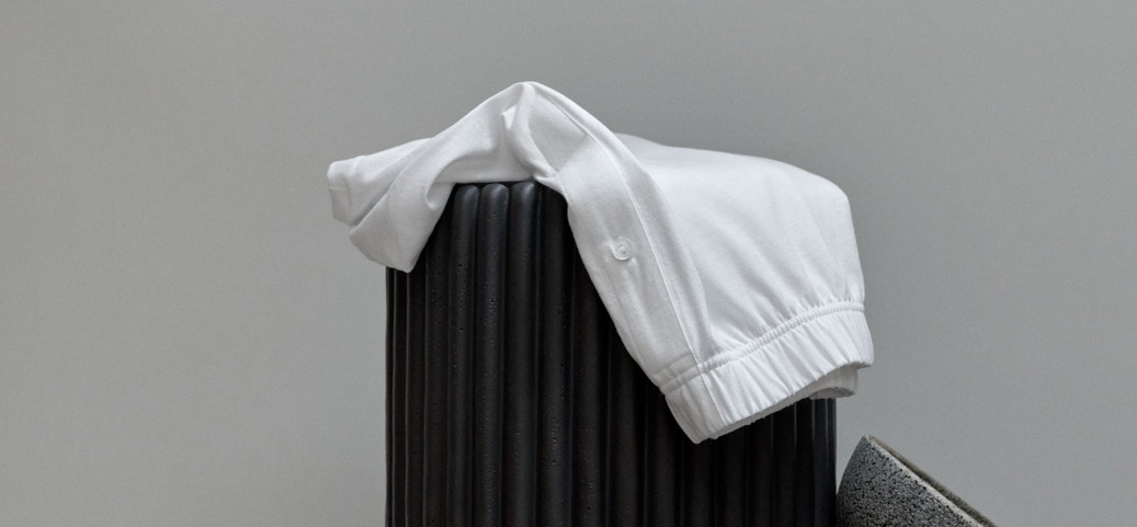 L'image montre un vêtement blanc drapé sur un objet noir de forme cylindrique. À côté, deux objets gris en forme de coupe sont empilés l'un sur l'autre.