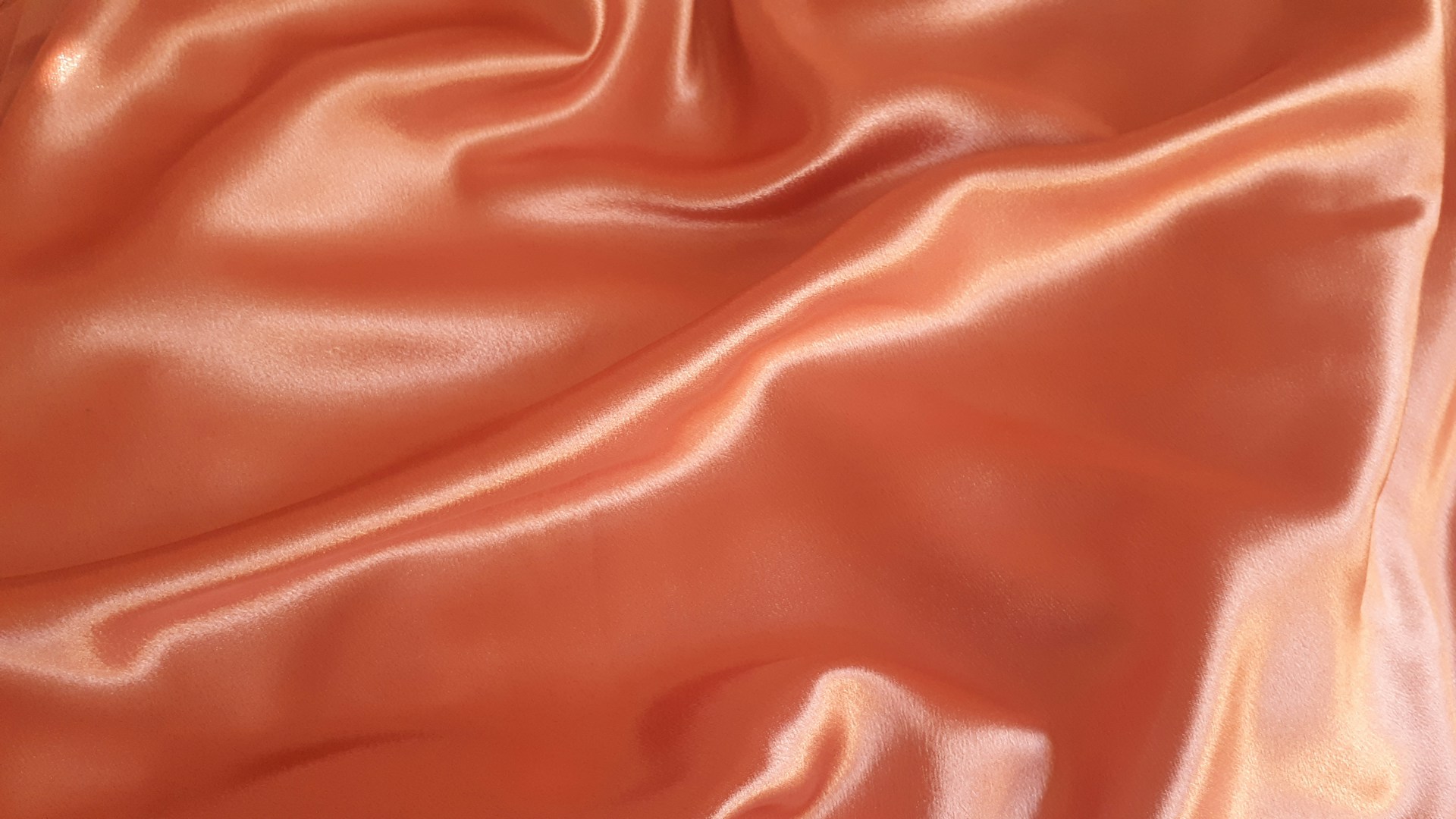 Gros plan sur un tissu en polyester de couleur orange, brillant avec des plis doux.
