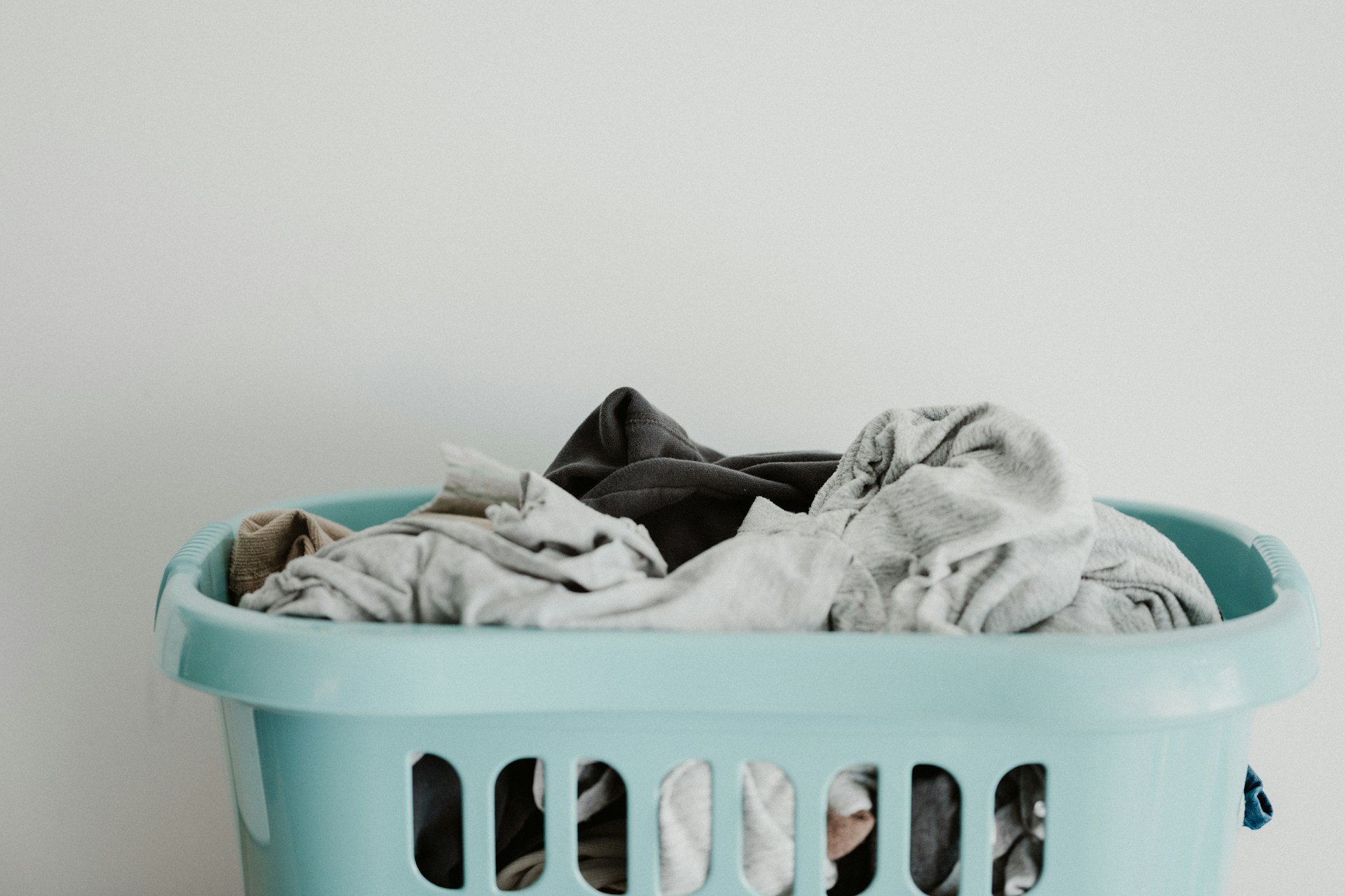 A turquoise laundry basket filled with clothes in neutral colours.