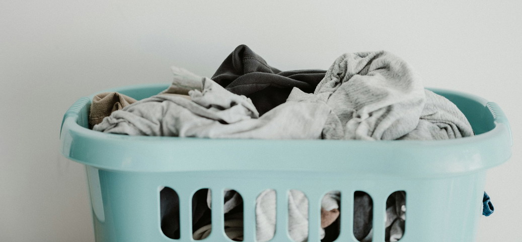 A turquoise laundry basket filled with clothes in neutral colours.