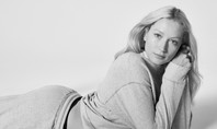 Frau liegt auf dem Boden und stützt sich mit ihren Ellbogen ab. Das Bild ist schwarz/weiss. Sie trägt einen graues Sweatshirt.