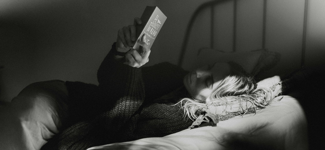 La personne est allongée dans un lit, détendue, et lit un livre dans une lumière faible afin de se calmer et de mieux s'endormir.