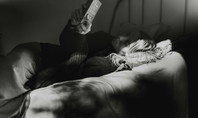 Person liegt entspannt in einem Bett und liest ein Buch im schwachen Licht, um zur Ruhe zu kommen und besser einschlafen zu können.
