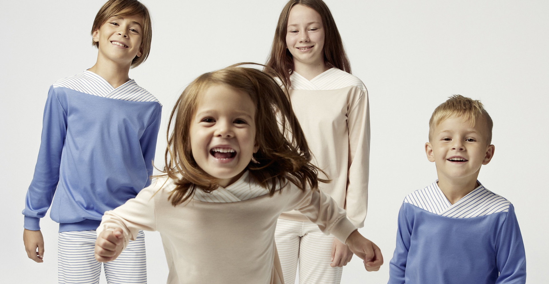 Vier Kinder in altersgerechten Schlafanzügen, die fröhlich in die Kamera schauen, symbolisieren den Schlafbedarf bei Kindern und die Bedeutung von bequemer Nachtkleidung für erholsamen Schlaf