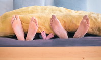 Parents et bébé en co-sleeping, leurs pieds dépassent ensemble de sous la couette.