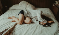 Auf dem Bild ist eine Frau zu sehen, die auf einem Bett ohne Kissen in einem dämmrigen Raum liegt.