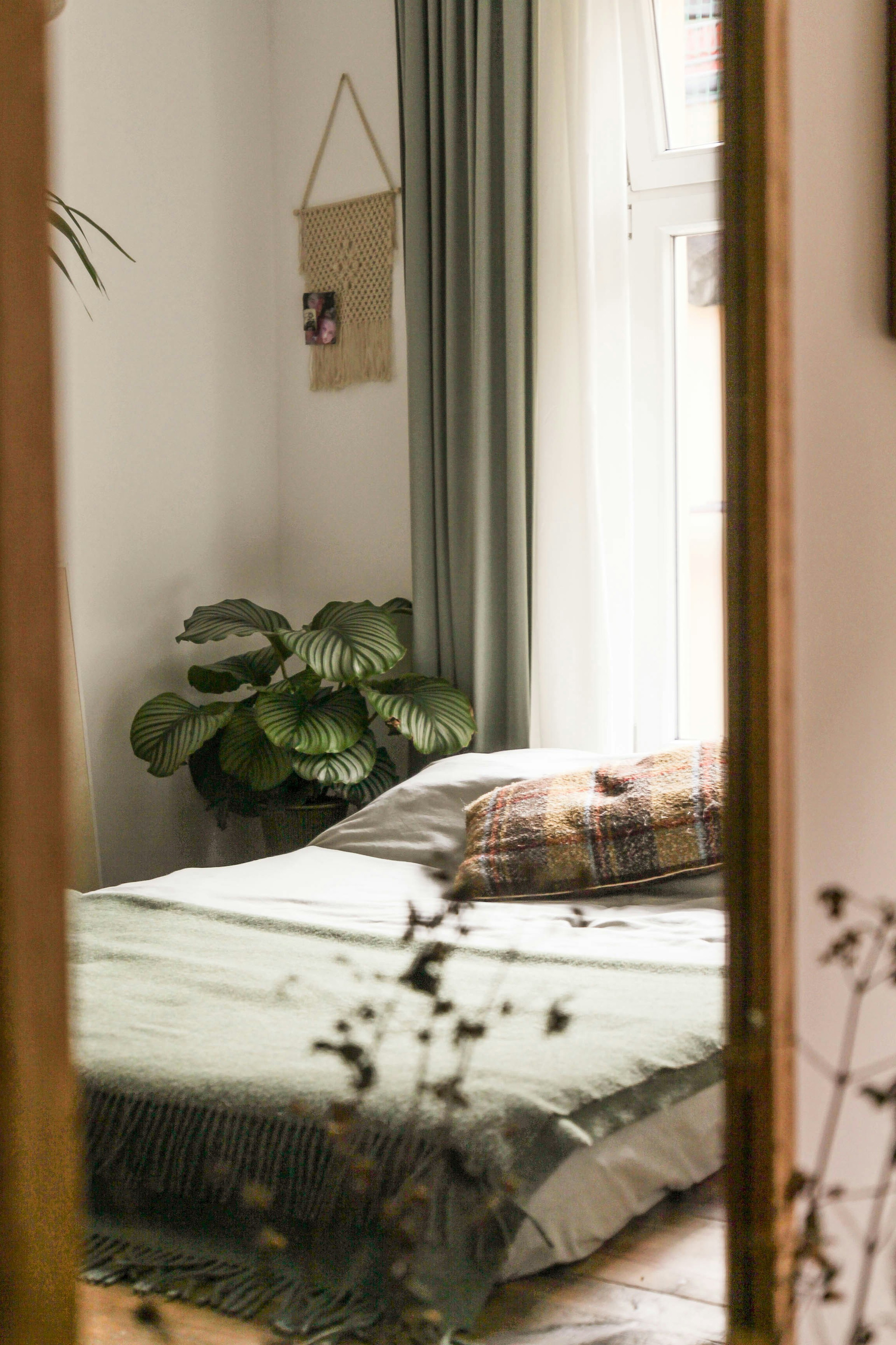 Ein Bett mit einer grünen Decke. Weisse Wandfarbe. Grüne Vorhänge.