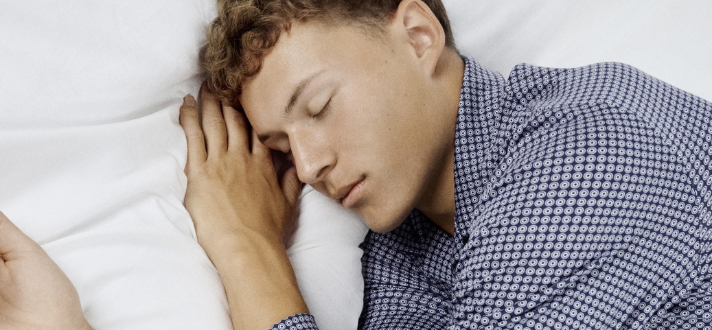 Un homme est allongé éveillé dans son lit, les yeux fermés, en accord avec la question : pourquoi ne puis-je pas dormir alors que je suis fatigué ?