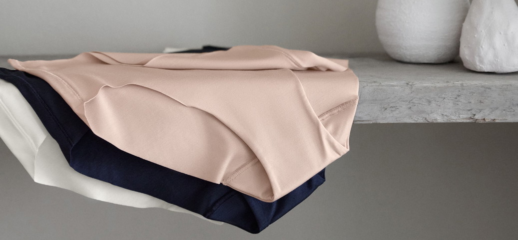 On y voit trois pantys de CALIDA de la série Natural Skin dans différentes couleurs, bien rangés sur une étagère.