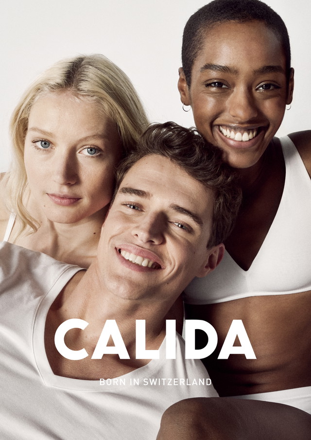 Trois mannequins souriants - une femme blonde, un homme brun et une femme à la peau foncée et aux cheveux courts - portent des basiques CALIDA blancs et posent serrés les uns contre les autres. L'inscription 'CALIDA - Born in Switzerland' est placée au-dessus de la photo.