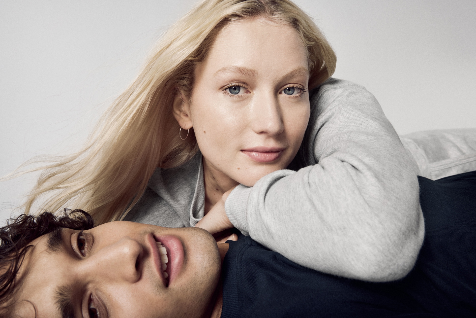 Un couple décontracté en vêtements CALIDA, présentant le Zwiebellook. La femme porte un pull gris, l'homme un haut foncé, tous deux ont l'air sereins et stylés.