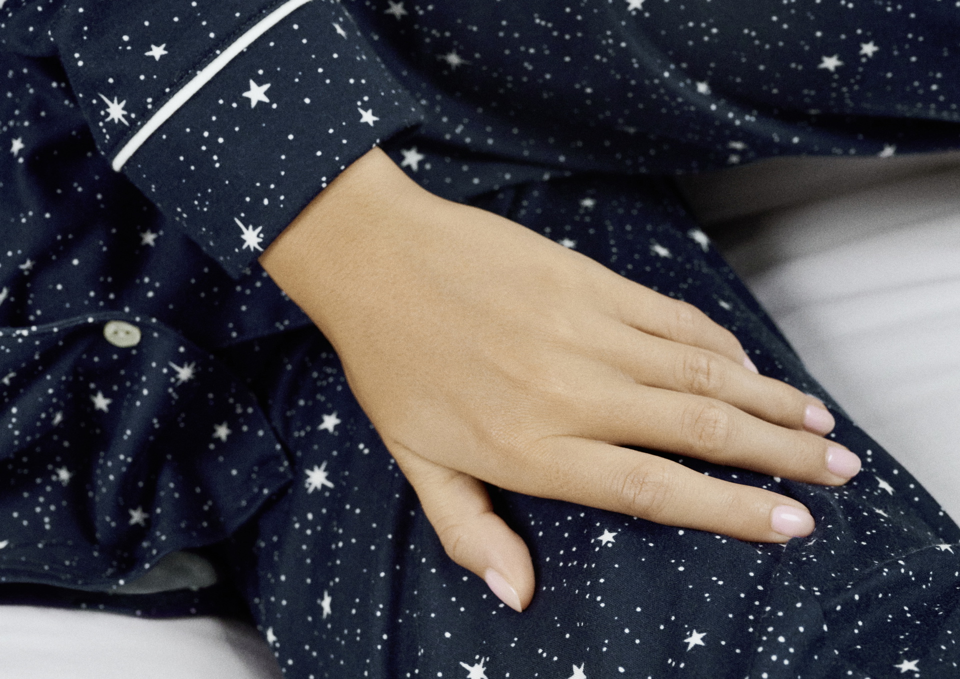 Gros plan d'une main sur un pyjama bleu foncé avec des motifs d'étoiles blanches.