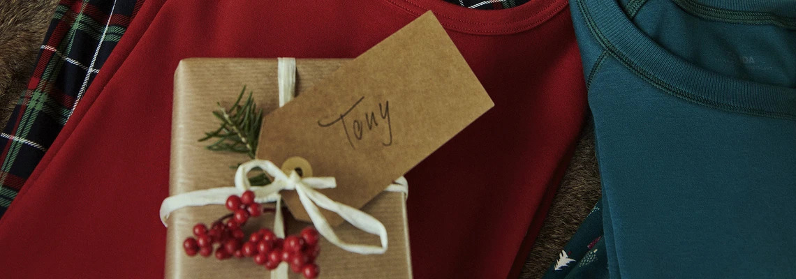 Petit cadeau emballé avec une étiquette au nom de 'Tony'. Le cadeau est posé sur des pyjamas de Calida.