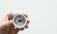 Une main tient un petit réveil blanc qui indique 3h10 - symbole de l'heure du coucher.