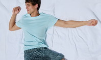 Un homme est allongé sur le dos et dort détendu dans un pyjama CALIDA bleu clair sur un lit blanc.
