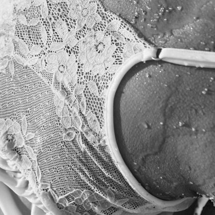 Close-up of a white lace top with a transparent structure and water droplets on the model's skin. Image in black and white.