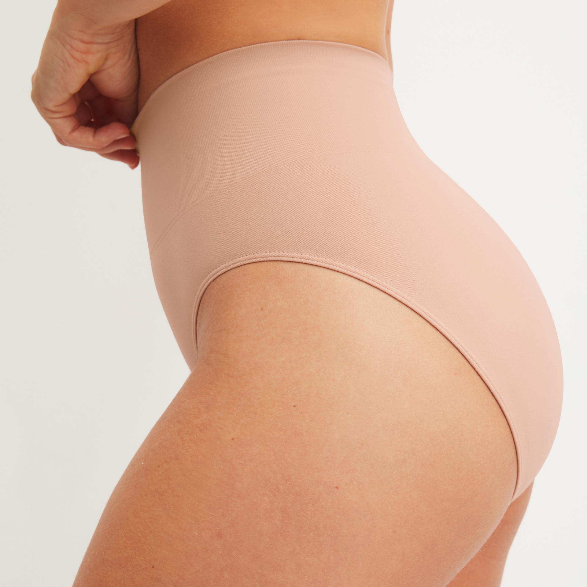 Woman wears shape-forming slip in nude with high leg cut and smooth surface for gentle shaping and comfort – side rear view