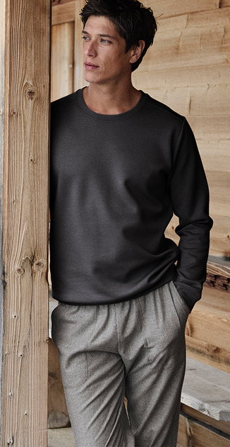 Le modèle porte un haut de pyjama gris foncé avec un col rond et un pantalon de détente gris dans un environnement naturel en bois.