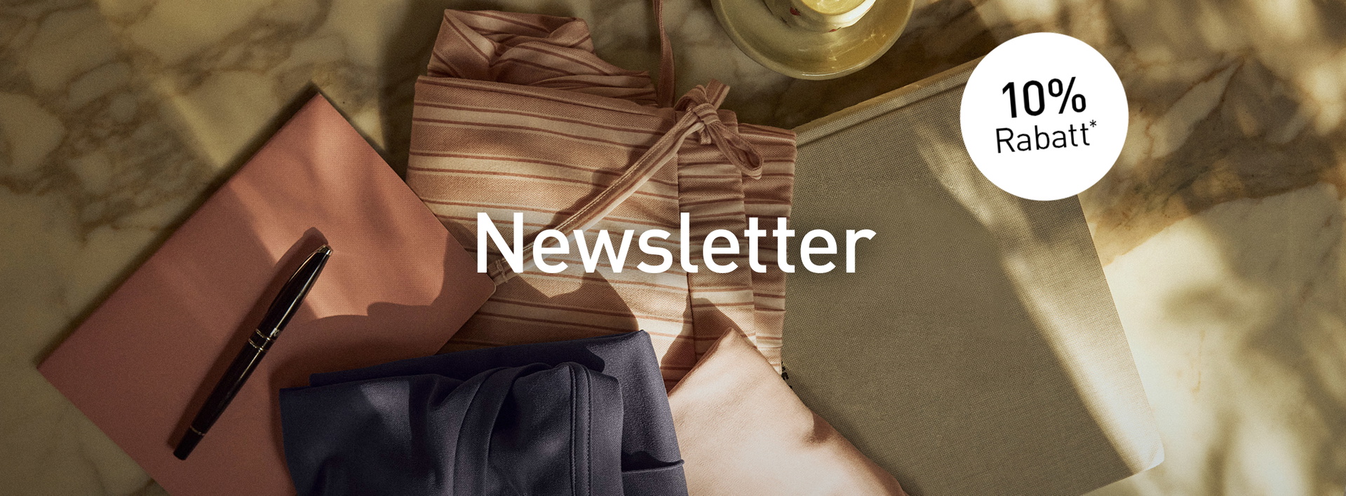 Gefaltete Loungewear- und Nachtwäsche-Styles in Rosa-, Blau- und Naturtönen auf Marmortisch mit Newsletter-Hinweis und 10 % Rabatt.